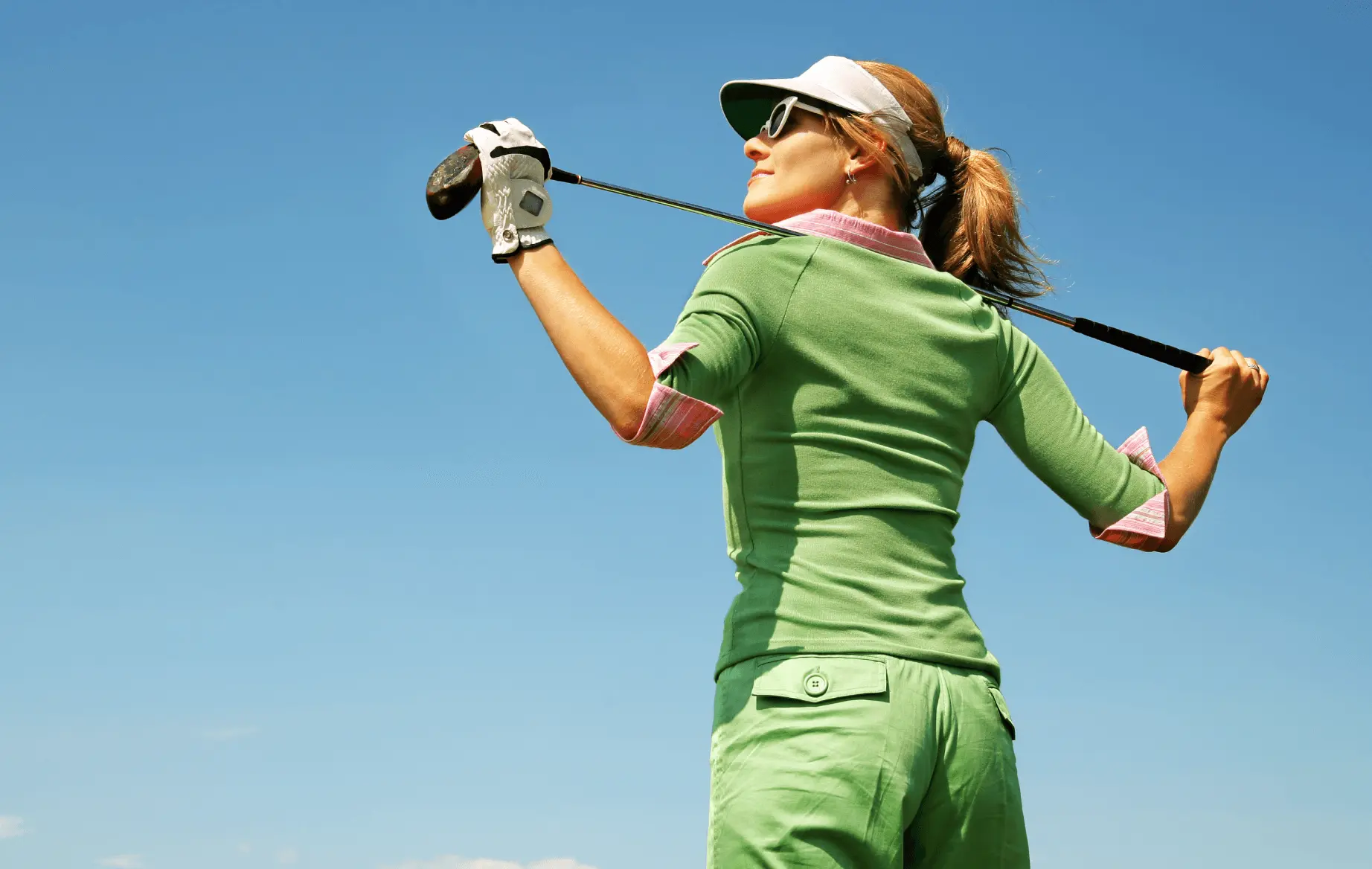 A woman stands on a golf course with her club across her shoulders.