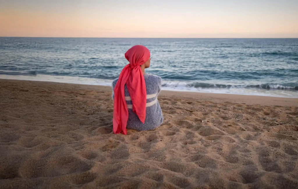 A woman sits at the beach looking out towards at the ocean.