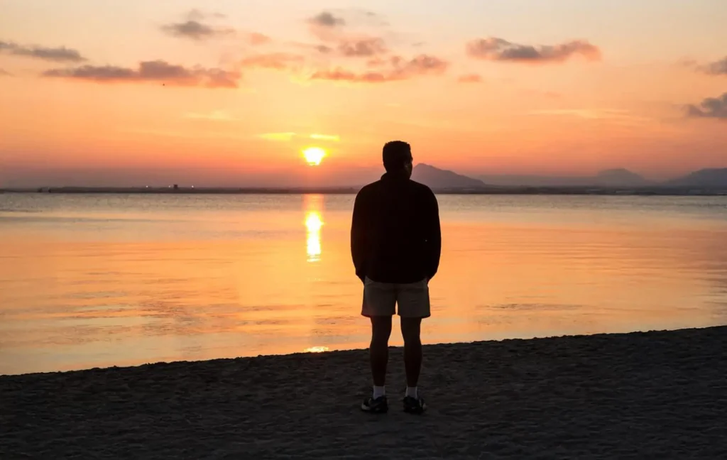 Person stands on the beach looking at a sunset.