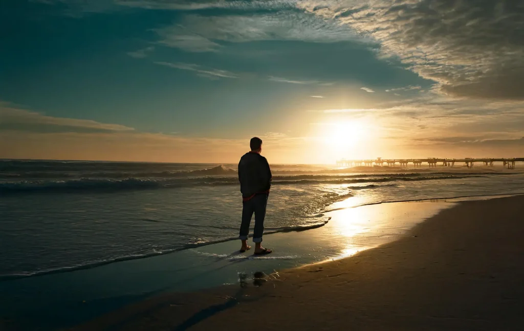 Person stands on the beach looking at a sunset.