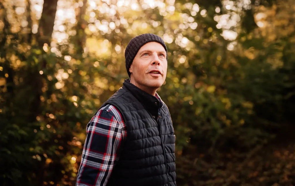 A man surrounded by trees gazes upwards.