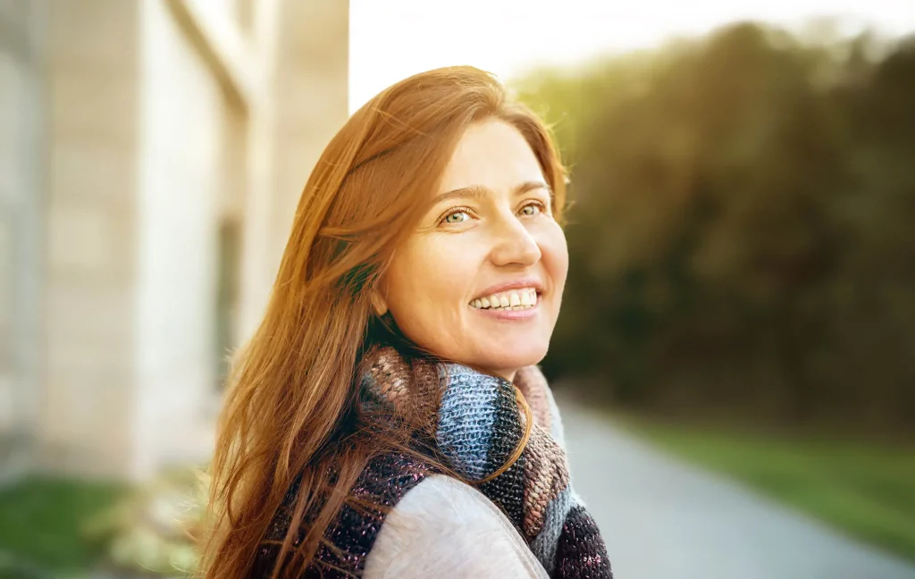 A smiling woman stands on a sidewalk.