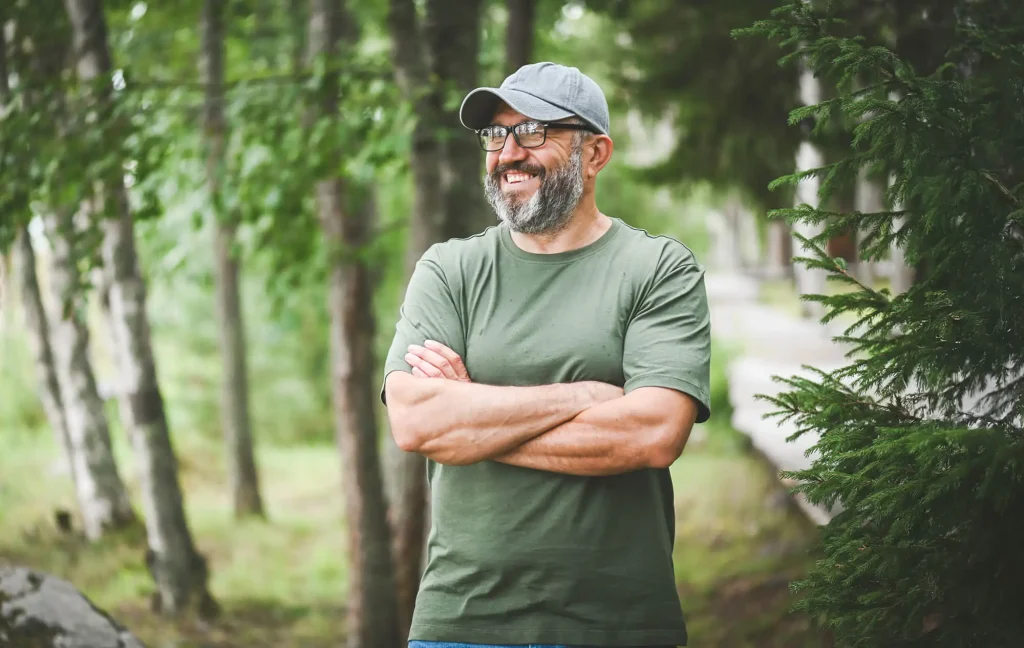 A smiling man stands in a forest.