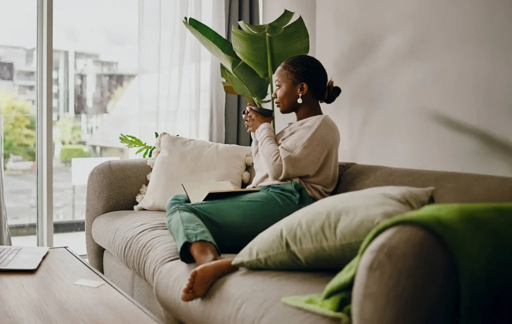 A woman sits on a couch and drinks coffee.