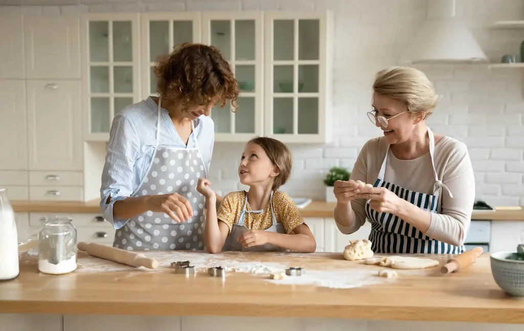 A grandmother, mother and granddaughter bake in the kitchen.